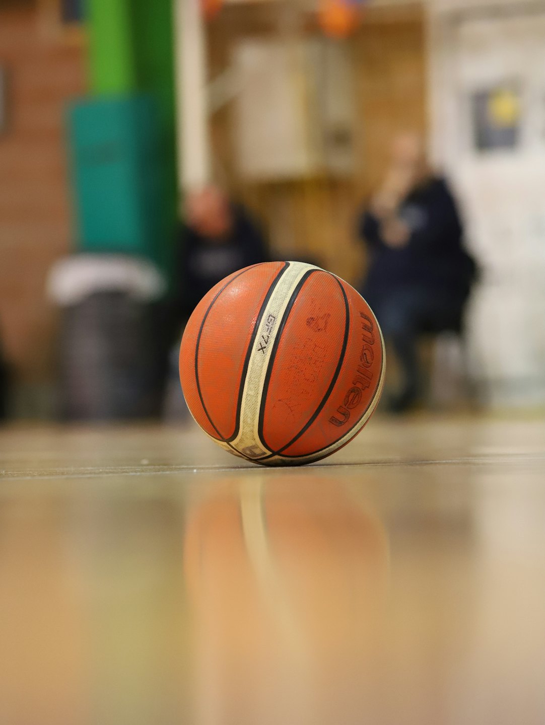 Un ballon de basket orange et blanc repose sur le parquet brillant d'un gymnase.